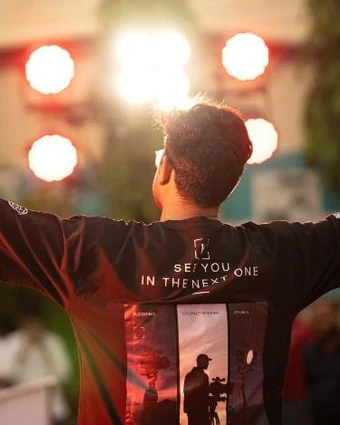 Back view on stage, arms spread under the stage lights, in a "See you in the next one" T-shirt